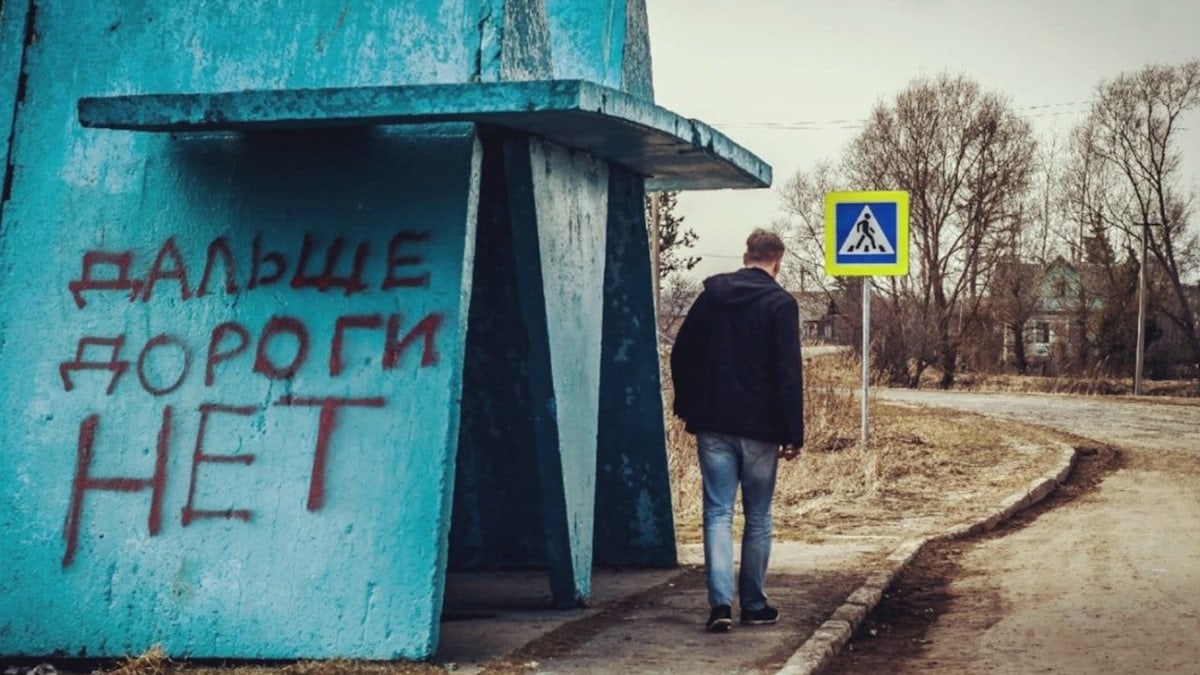 a man walking down a dirt road next to a blue building