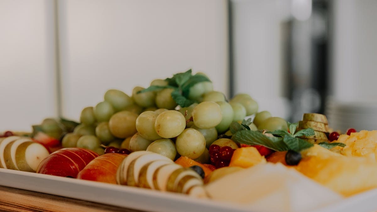 A vibrant assortment of fruits including grapes, apples, and berries on a white tray.